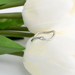 Silver ring with a small diamond on a white tulip with green leaves.