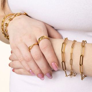 Gold jewelry including bracelets and rings on a person's wrist and hand against a white background.