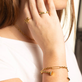 Close-up of a hand wearing gold rings and bracelet on a neutral background