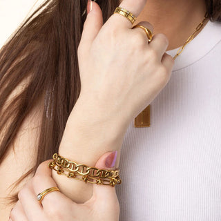 Close-up of a hand wearing gold jewelry including a bracelet, ring, and necklace on a white background.