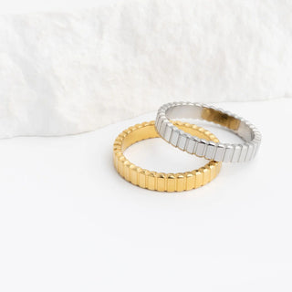 Two gold rings with a textured band design on a white background
