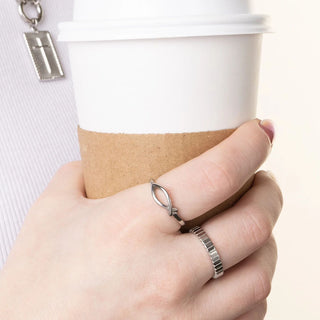 Hand holding a coffee cup with a close-up of a silver ring on a light background