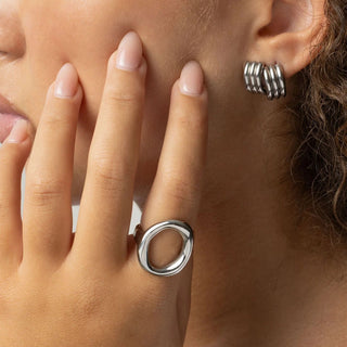 Close-up of a person wearing silver hoop earrings and a ring on a neutral background