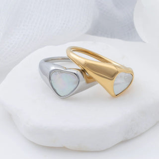 Two heart-shaped rings, one gold and one silver, on a white stone surface.