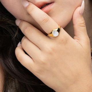 Close-up of a hand wearing a gold ring with a heart-shaped MOP, touching hair.