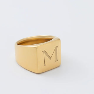 Gold square signet ring with 'M' on a light gray background