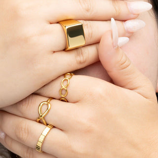 Close-up of hands wearing gold rings on a neutral background
