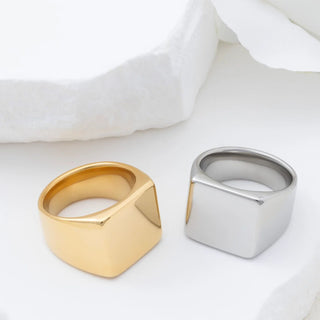 Gold and silver square-shaped signet rings on a white fabric background