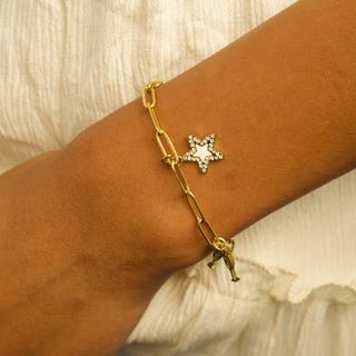 Gold bracelet with star charm on a wrist against a neutral background