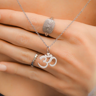 Hand wearing a silver ring with a sun design and a necklace with an Om symbol pendant.
