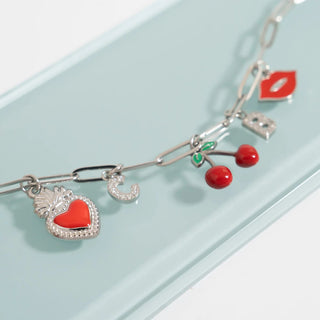 Silver bracelet with charms including a red heart, moon, and cherries on a light blue background