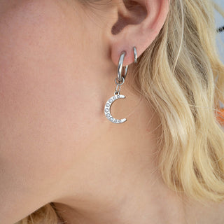 Silver hoop earring with a moon-shaped charm worn by a person with blonde hair.