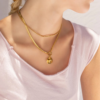 Gold necklace with a cowboy hat  pendant on a person wearing a white top