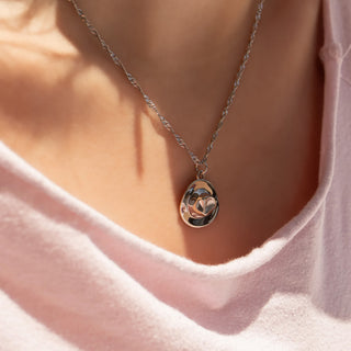Necklace with a cowboy hat pendant worn by a person in a pink shirt