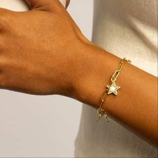 Hand holding a white vase with gold jewelry on a neutral background
