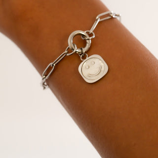 Silver bracelet with a smiley face charm on a wrist against a neutral background