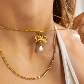 Gold necklace with a bow and pearl pendant worn by a person.