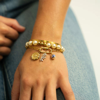 Close-up of a hand wearing multiple gold and pearl bracelets with charms.