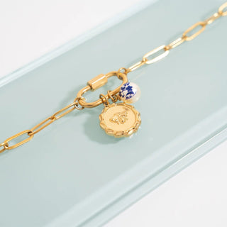 Gold bracelet with two charms on a light blue background