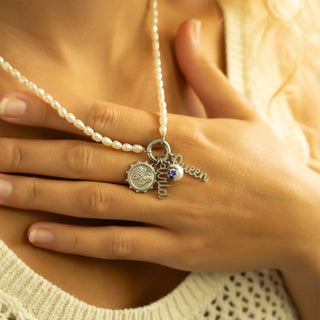 Pearl necklace with charms held by a hand against a blurred background