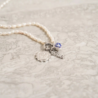 Pearl necklace with silver charms on a textured white surface