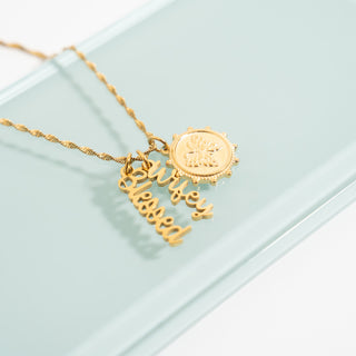 Gold necklace with 'blessed' pendant on a light green background