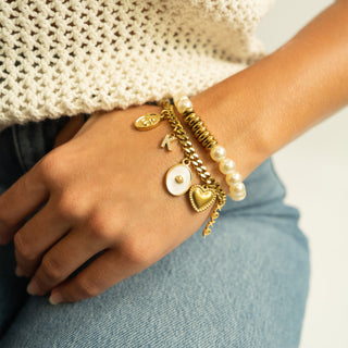Close-up of a wrist wearing multiple gold and pearl bracelets with charms including the shell design charm.