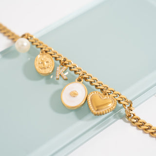 Gold bracelet with various charms  including the shell design charm on a light blue background