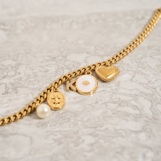 Gold bracelet with various charms  including the shell design charm on a light gray surface