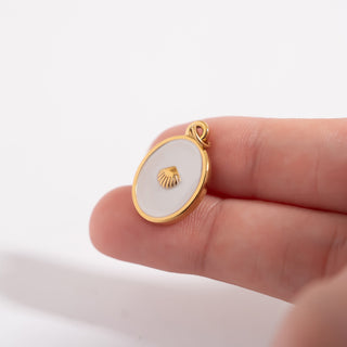 Gold pendant with a shell design held between fingers for scale on a white background