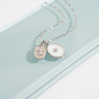 Silver necklace with two round pendants  including the shell design charm on a light blue background