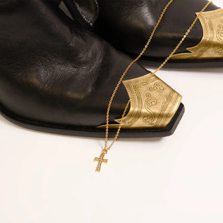 Gold necklace with a cross pendant on a black cowboy boots with gold accents.