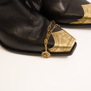 Gold shoe charm on a black shoe with a white background