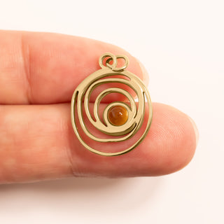 Gold spiral pendant with a central gemstone held between fingers on a white background