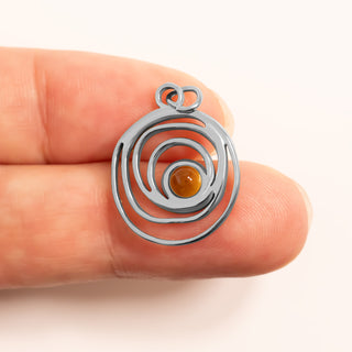 Silver spiral pendant with a yellow stone held between fingers on a white background