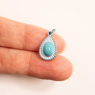 Turquoise stone pendant held between two fingers for scale against a white background