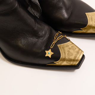 Turquoise Star Charm near gold toed black leather cowboy boots on a white background