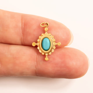 Gold pendant with a turquoise stone held between two fingers for scale on a white background