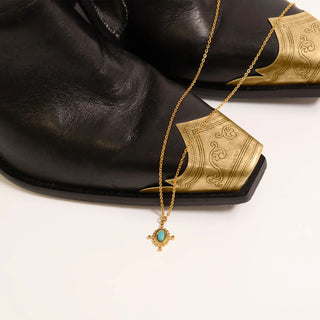 Gold necklace with the Turquoise Compass Charm on  black leather cowboy boots