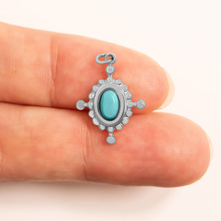 Silver compass pendant with turquoise stone held between two fingers for scale on a white background