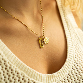 Gold necklace with heart-shaped pendant on a person wearing a beige sweater.