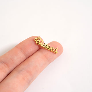 Gold 'blessed' charm held between fingers on a white background