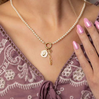 Pearl necklace with a gold pendant worn by a person in a patterned top.