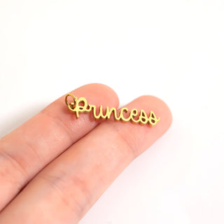 Gold 'Princess' charm held between fingers on a white background