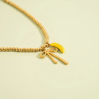 Gold beaded necklace with a yellow bow and banana charm on a light green background