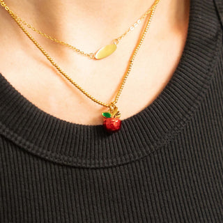 Gold beaded necklace with a red apple pendant on a black sweater