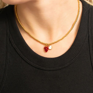 Gold beaded necklace with heart-shaped pendants worn by a person against a black background