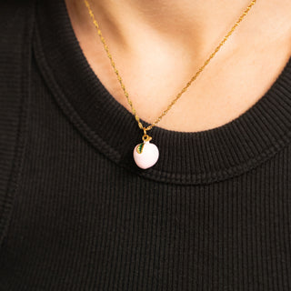 Necklace with a pink peach pendant worn by a person wearing a black sweater