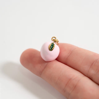 Small pink peach charm with a gold and green center held between fingers on a white background for scale