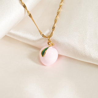 Necklace with a pink peach pendant and gold chain on a beige fabric background